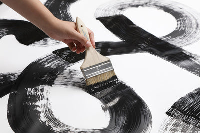 A hand holding a paintbrush applying a wide stroke of black paint.